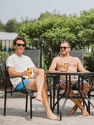 Two guys drinking beer in patio chairs at the pool