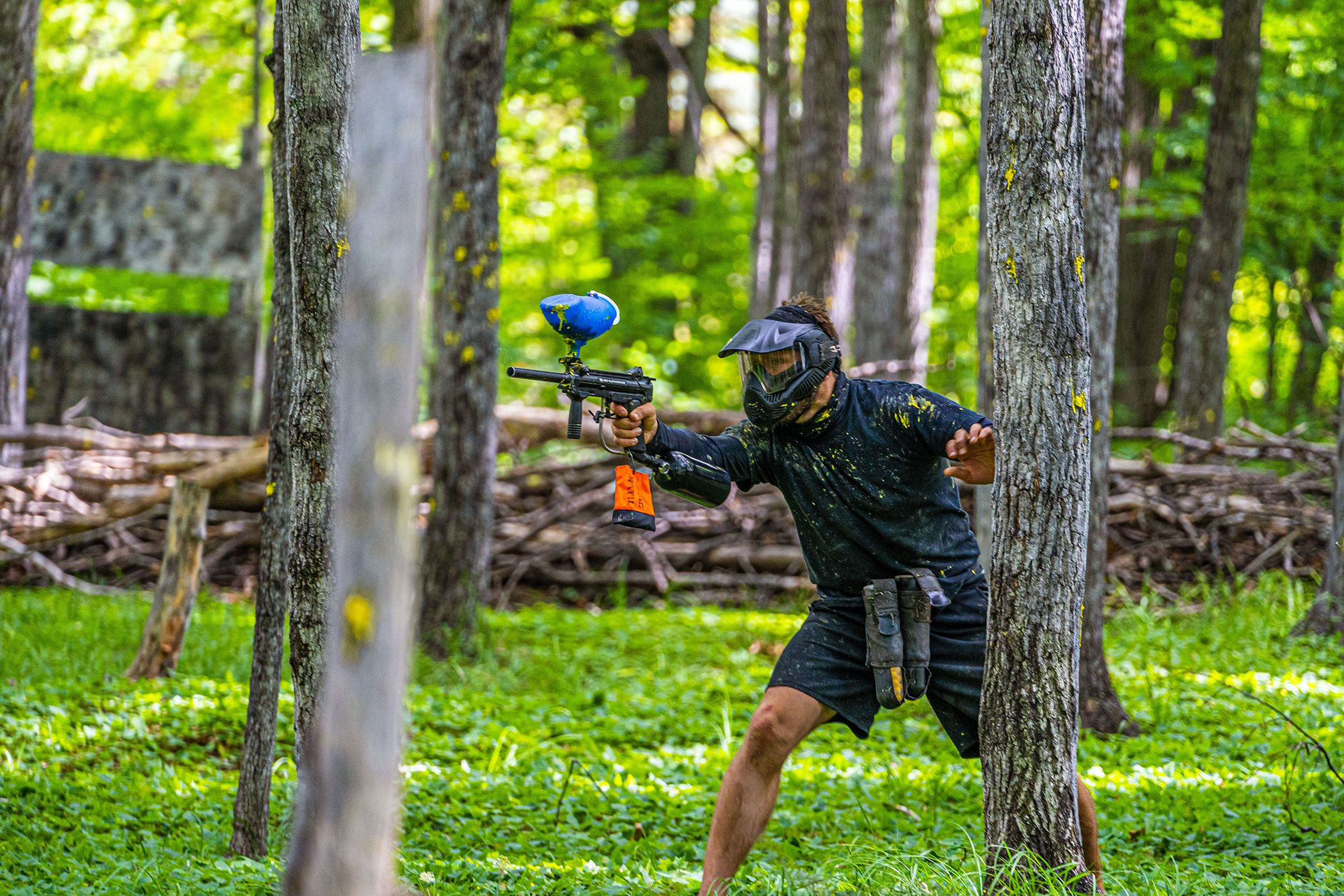 Man hiding behind tree with paintabll gun ready to shoot.