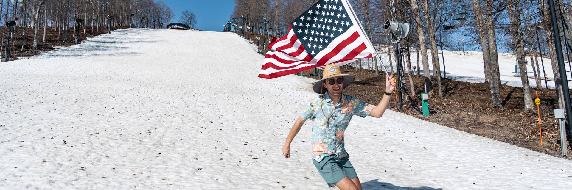 guy skiing down hill in summer clothes holding american flag