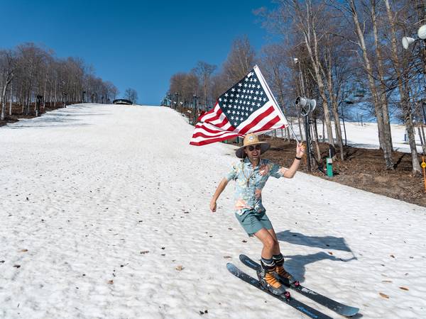 guy skiing down hill in summer clothes holding american flag