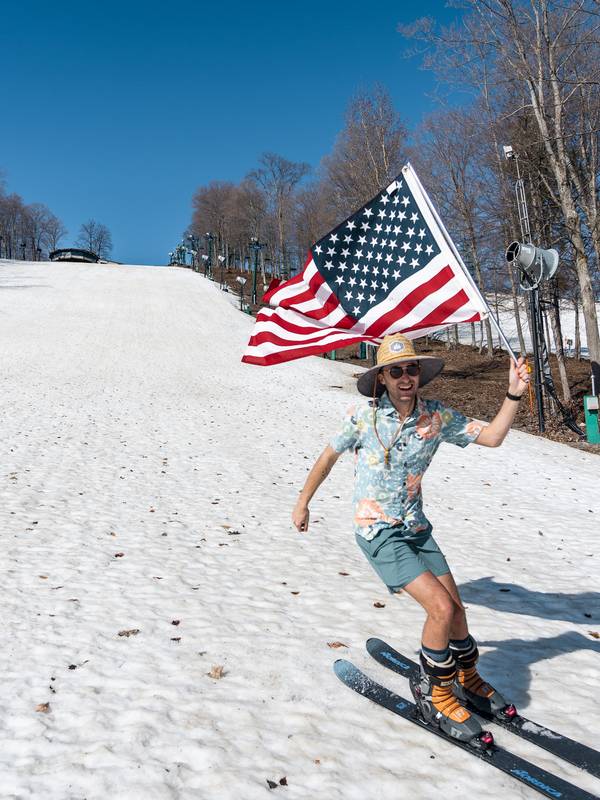 guy skiing down hill in summer clothes holding american flag
