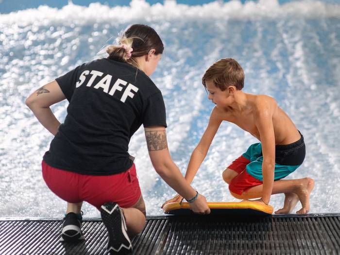 Staff helping child on surf simulator