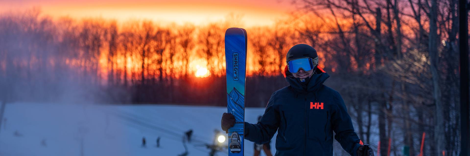 man holding skis at summit at sunset