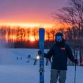 man holding skis at summit at sunset