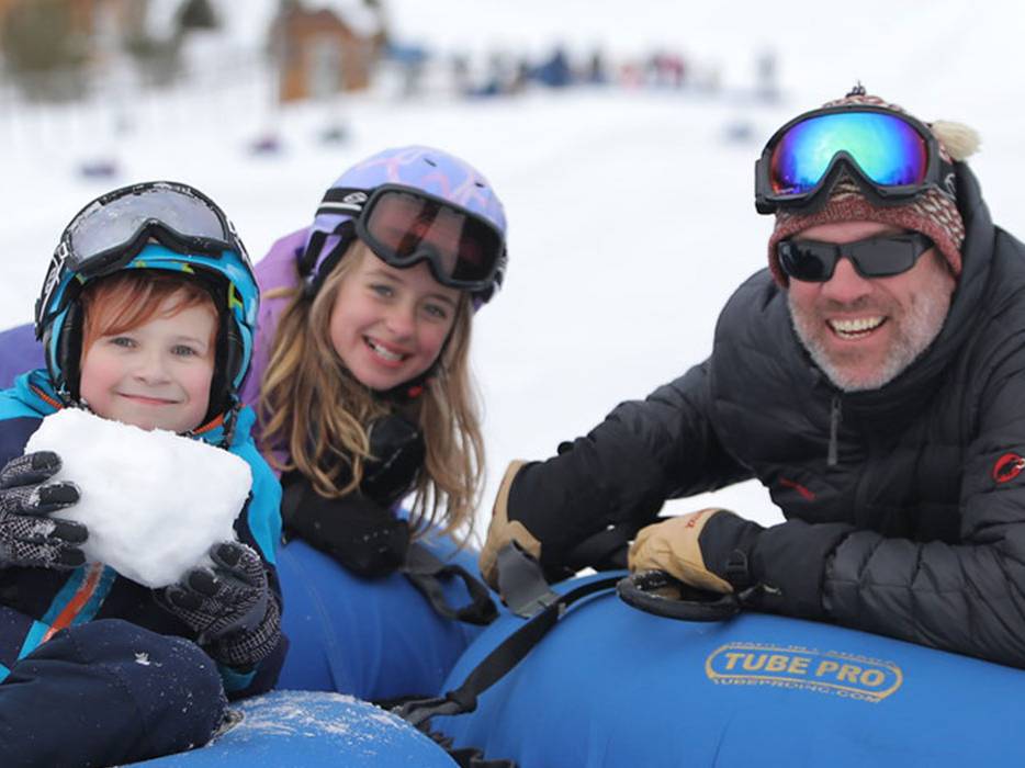 Dad and two kids on tubes with son holding a block of snow