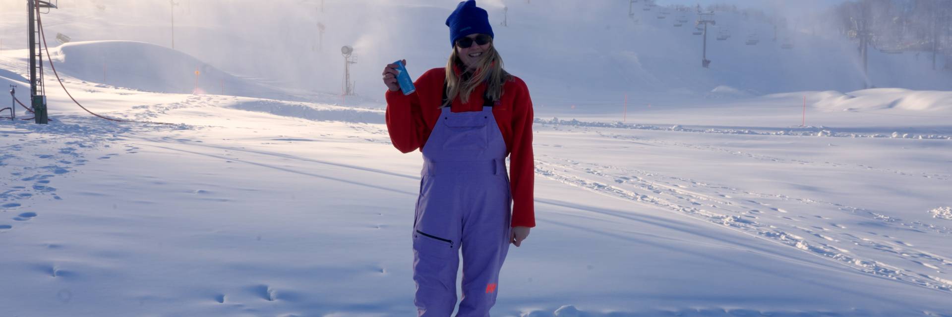 Woman holding red bull in front of ski slope