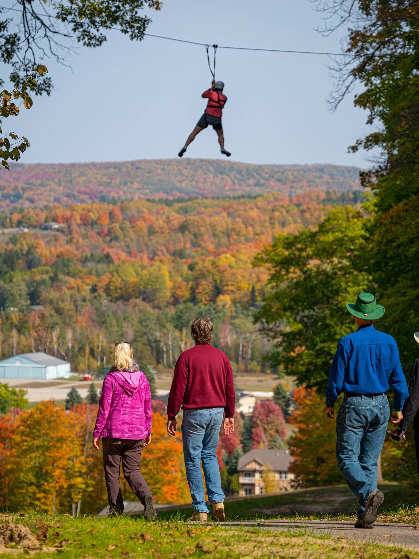 People walking while a person is ziplining thorugh the air during the fall