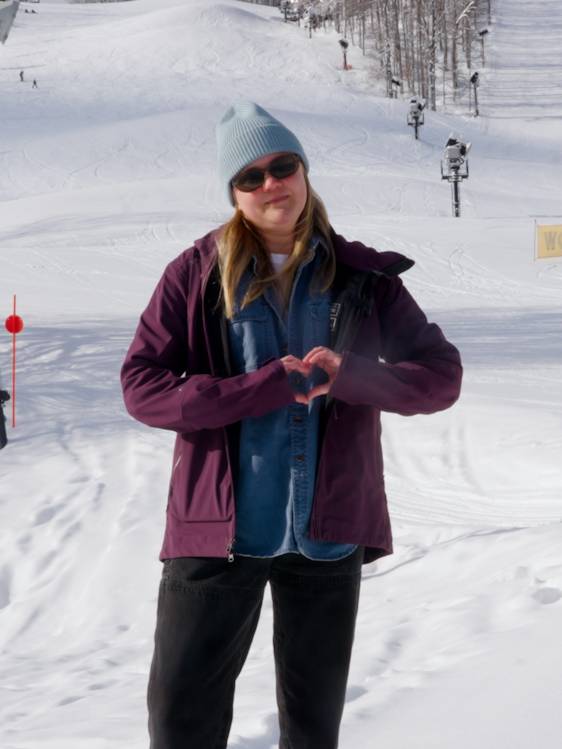 Woman standing at the base of Mountain making a heart with hands
