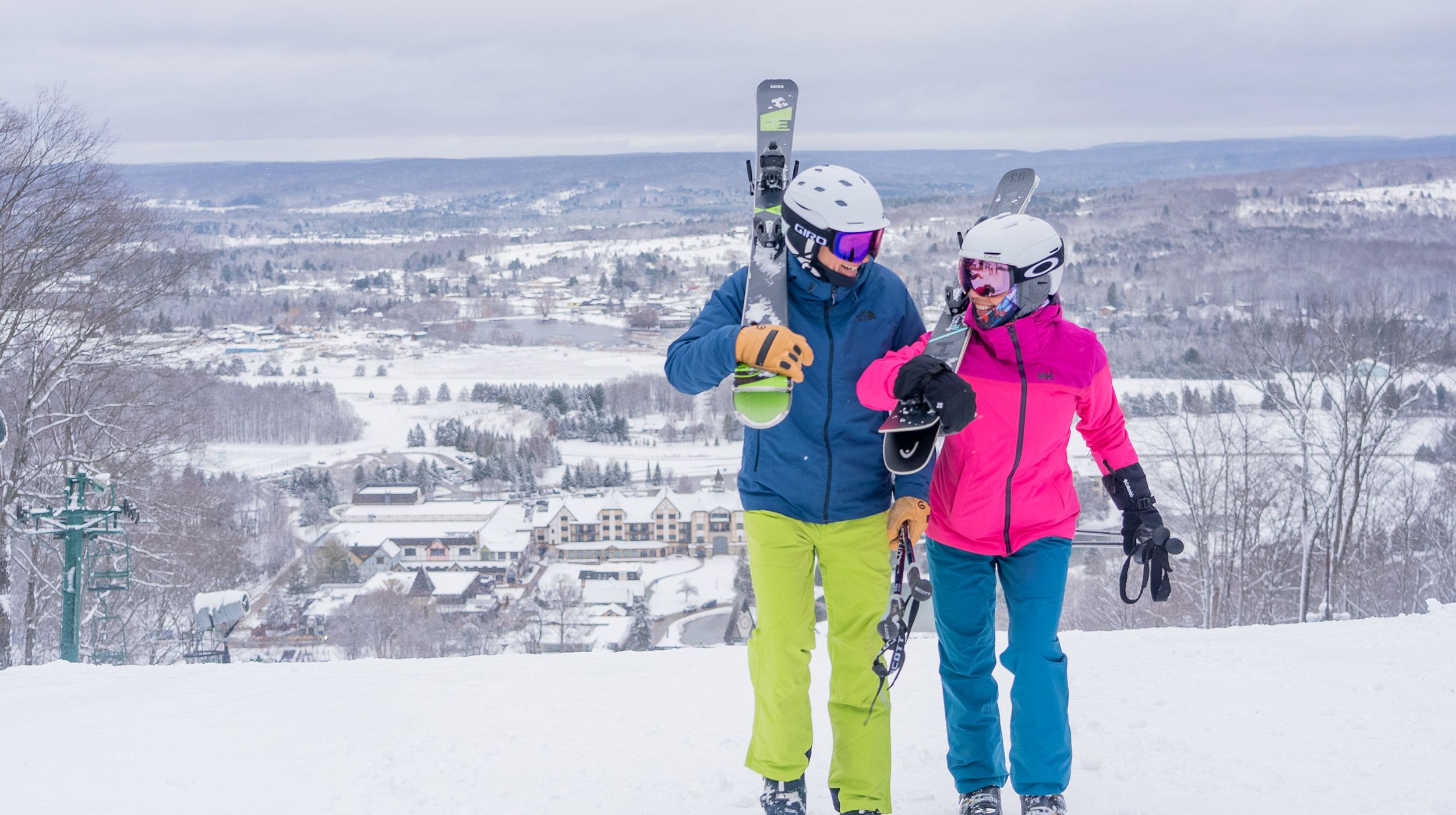 Couple walking with skis on shoulder walking on the top of hill