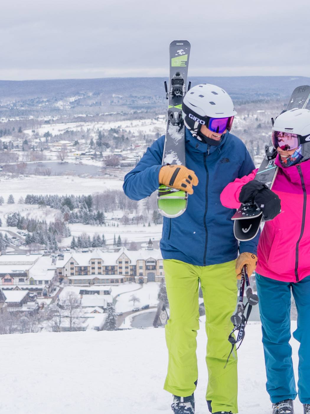 Couple walking with skis on shoulder walking on the top of hill