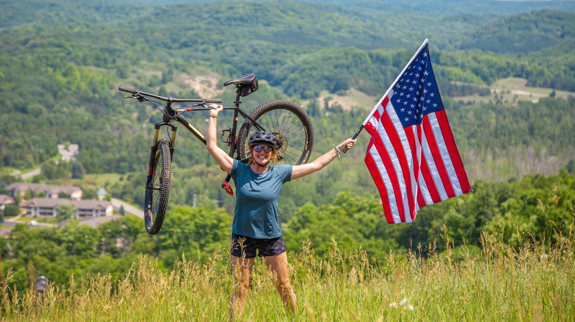girl holding up American flag and her mountain bike on top of the Hemlock