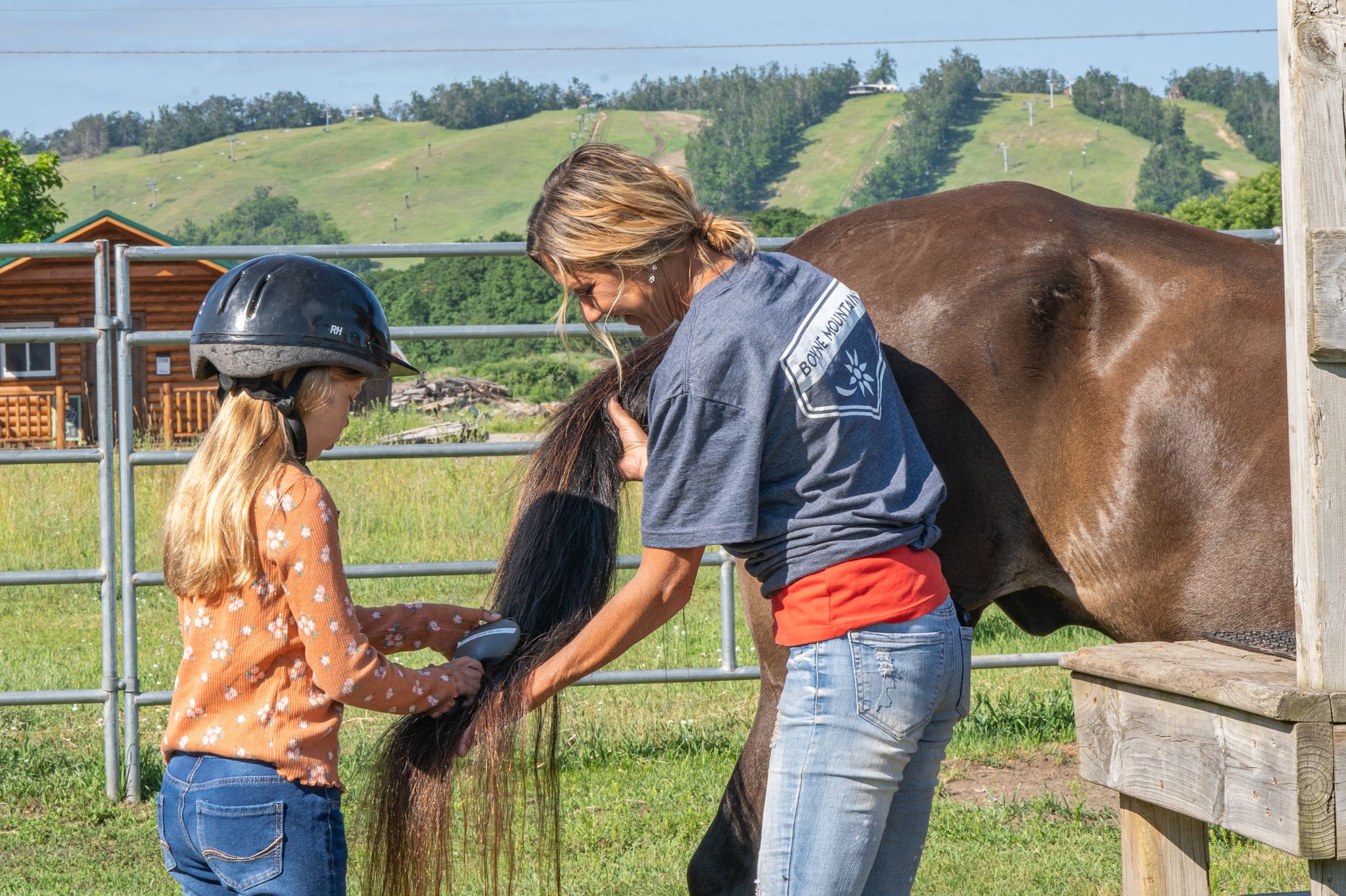 Child brushing horse tail with wrangler
