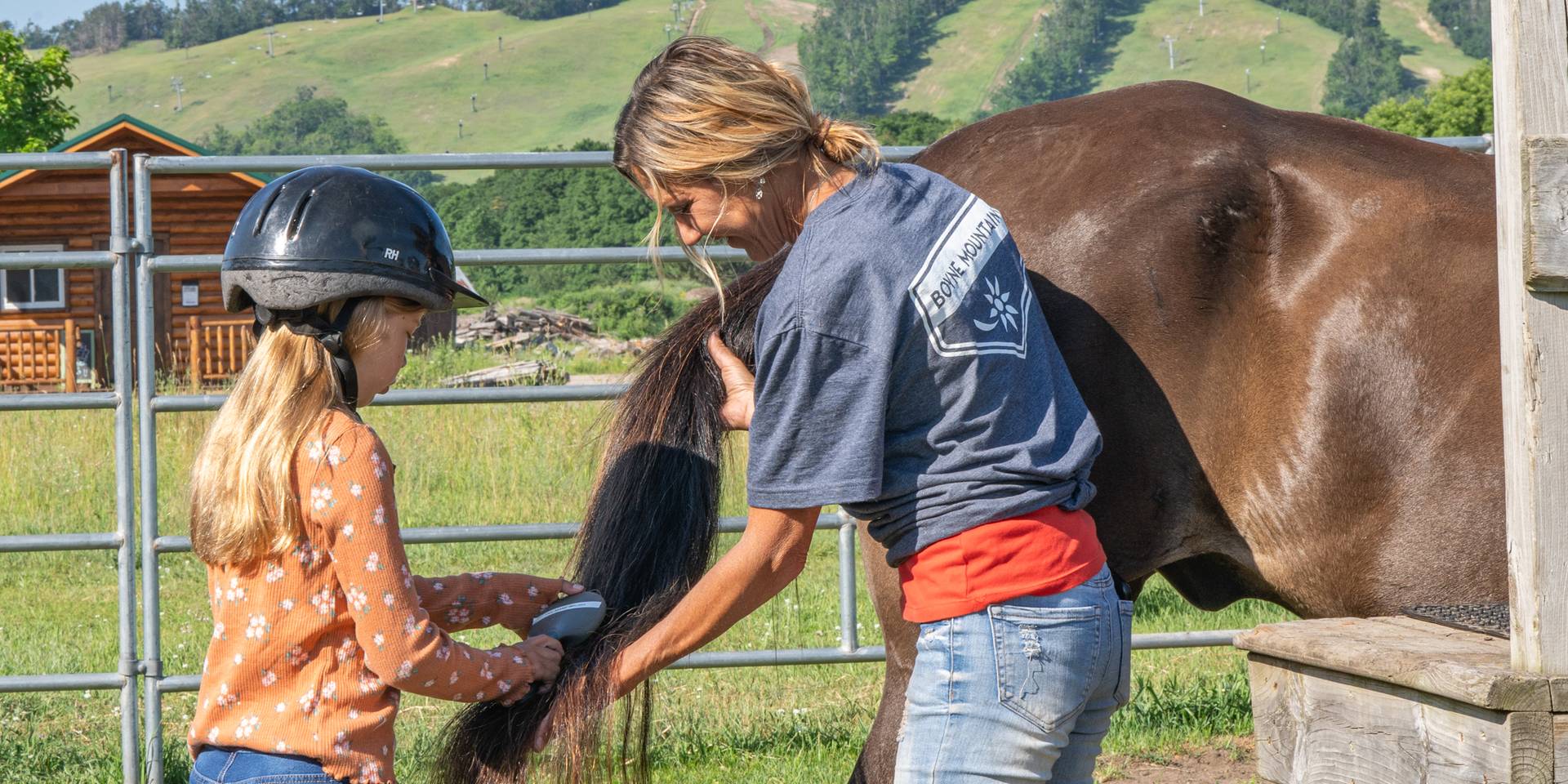 Child brushing horse tail with wrangler