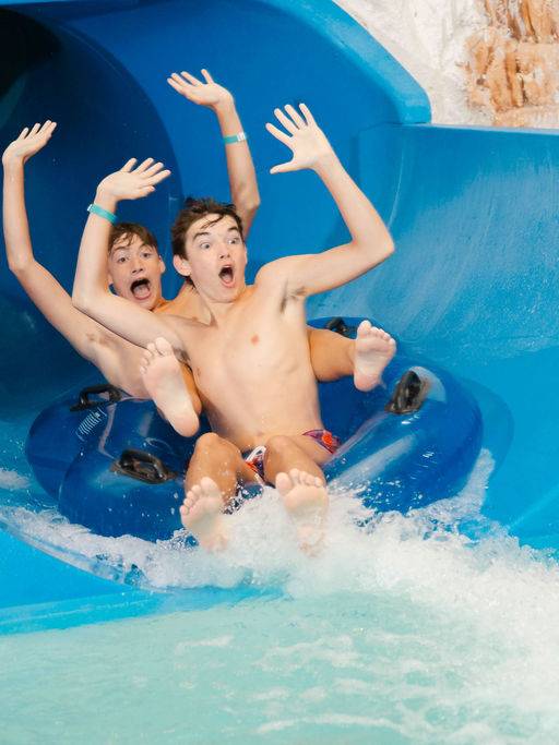 Two boys on tube riding down water slide with hands up in the air