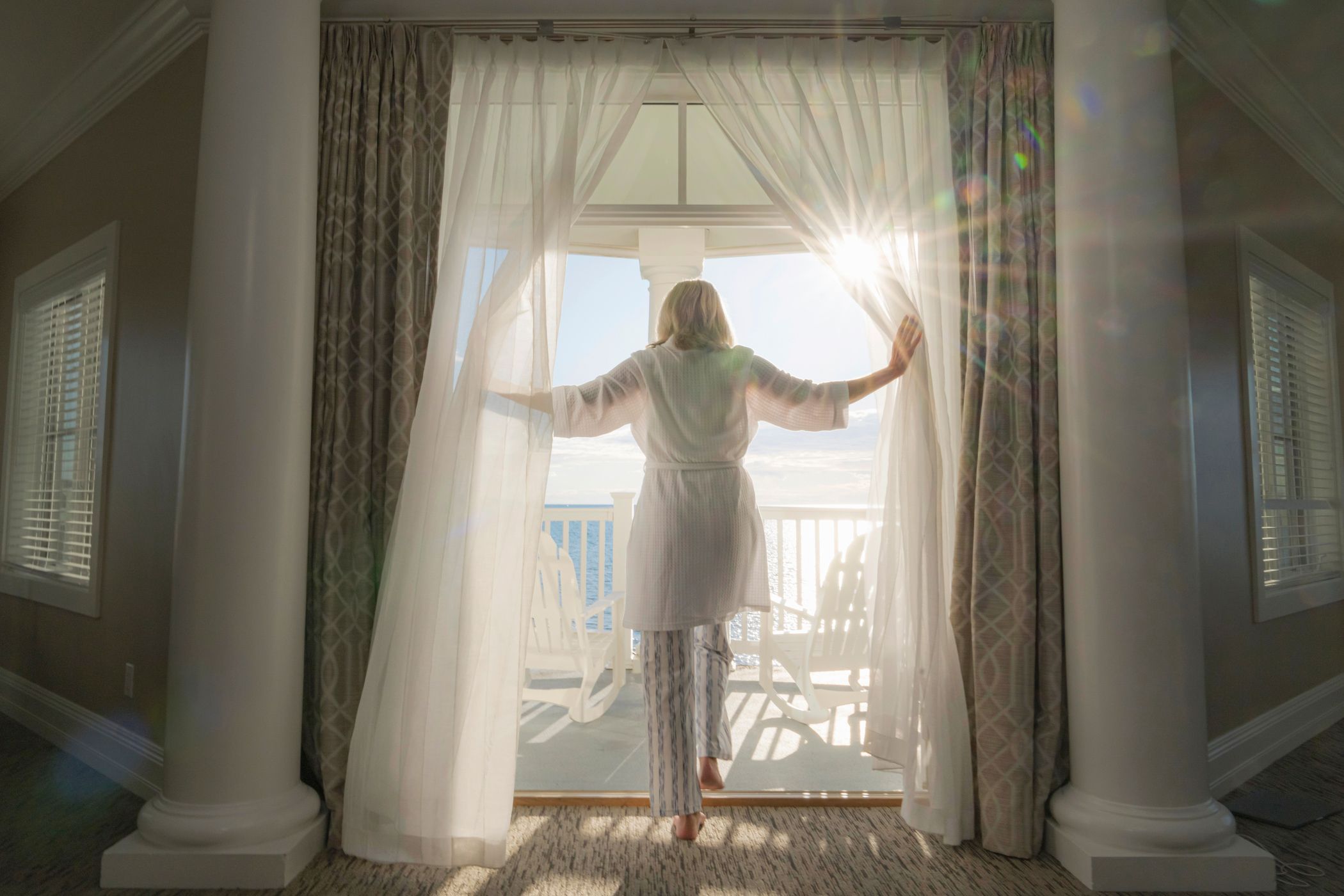Woman stepping out onto morning lakefront balcony