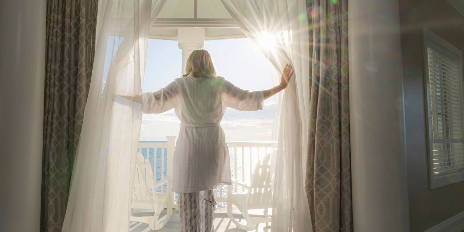 Woman stepping out onto morning lakefront balcony