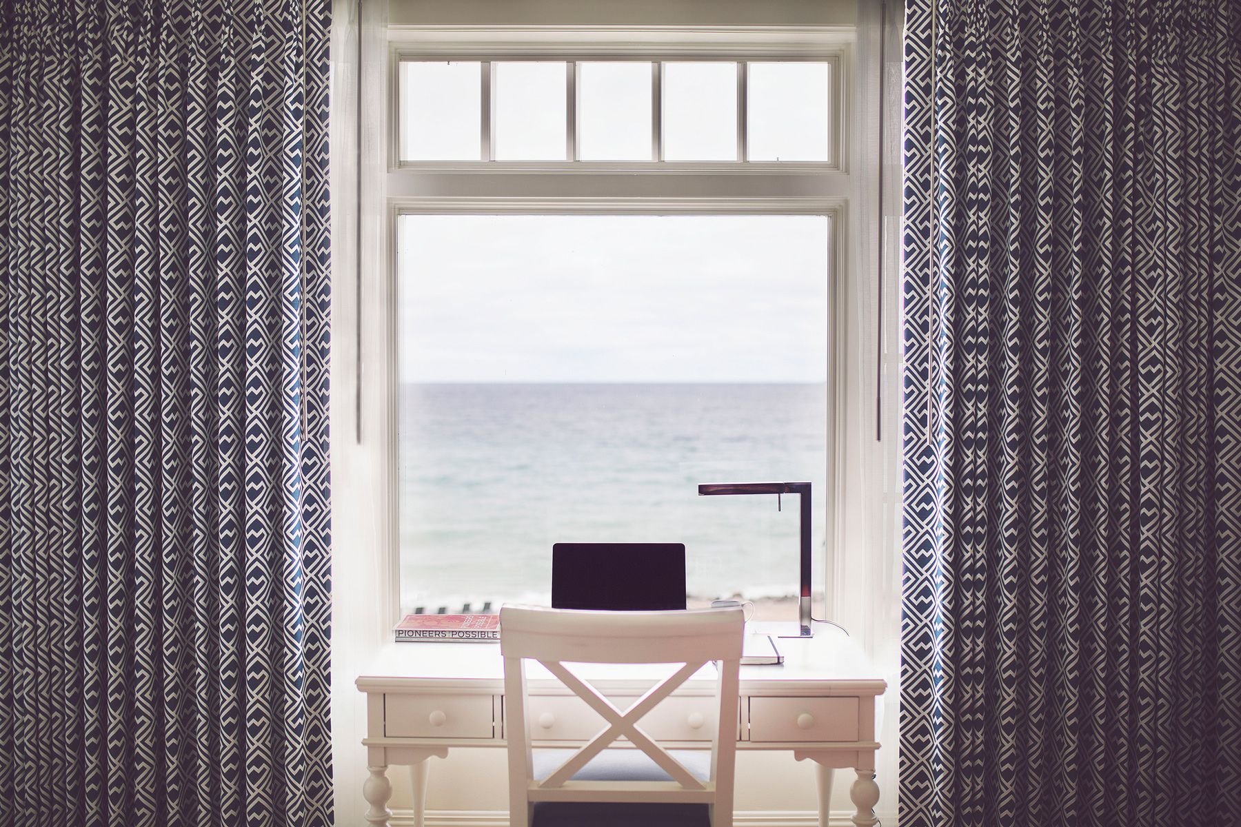 A wide view of a computer at a hotel room desk overlooking blue water