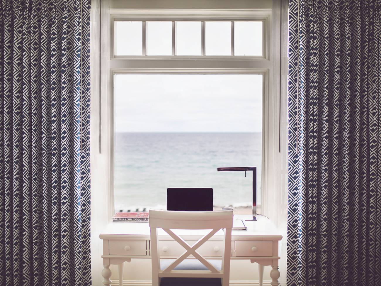 A wide view of a computer at a hotel room desk overlooking blue water