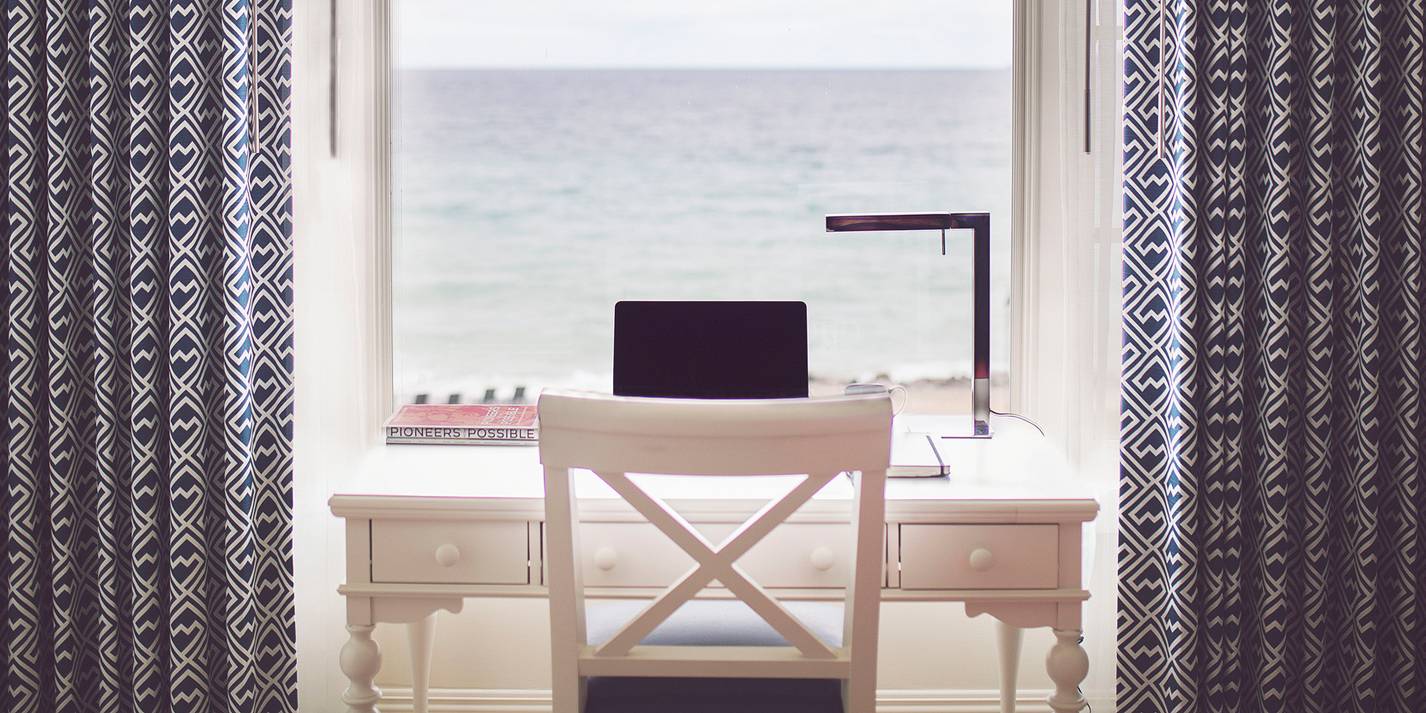 A wide view of a computer at a hotel room desk overlooking blue water