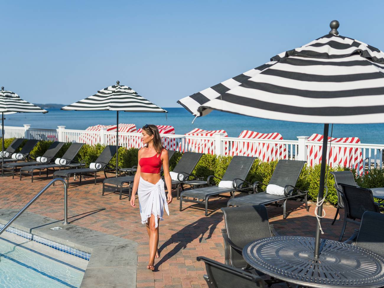 Young woman walking along pool deck near umbrellas and beach, Inn at Bay Harbor