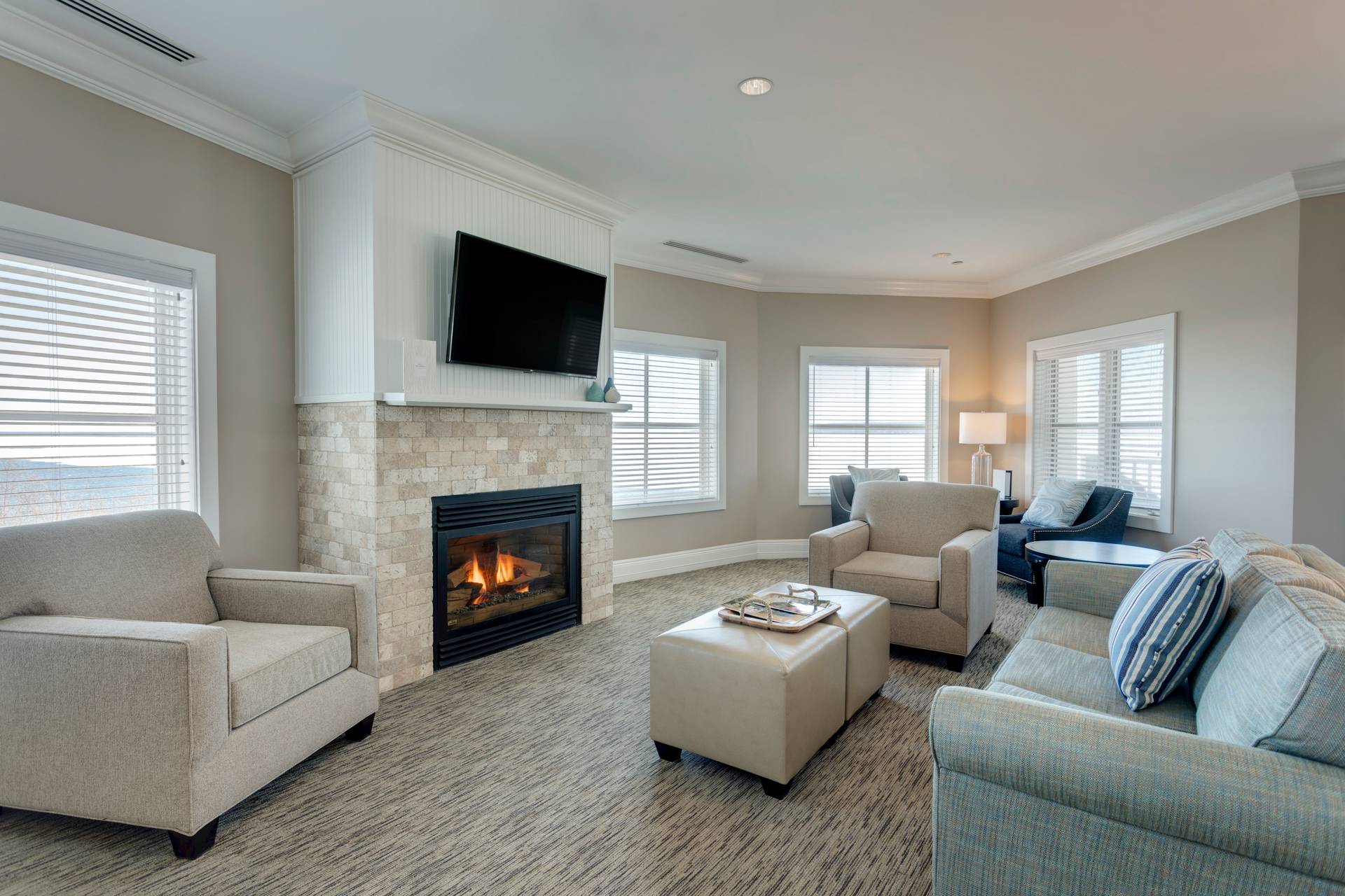 Open living area with stone fireplace, neutral couches in front of large square windows