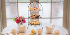 Afternoon Tea table setup with flowers, tea pots, tiered tray of treats and finger sandwiches