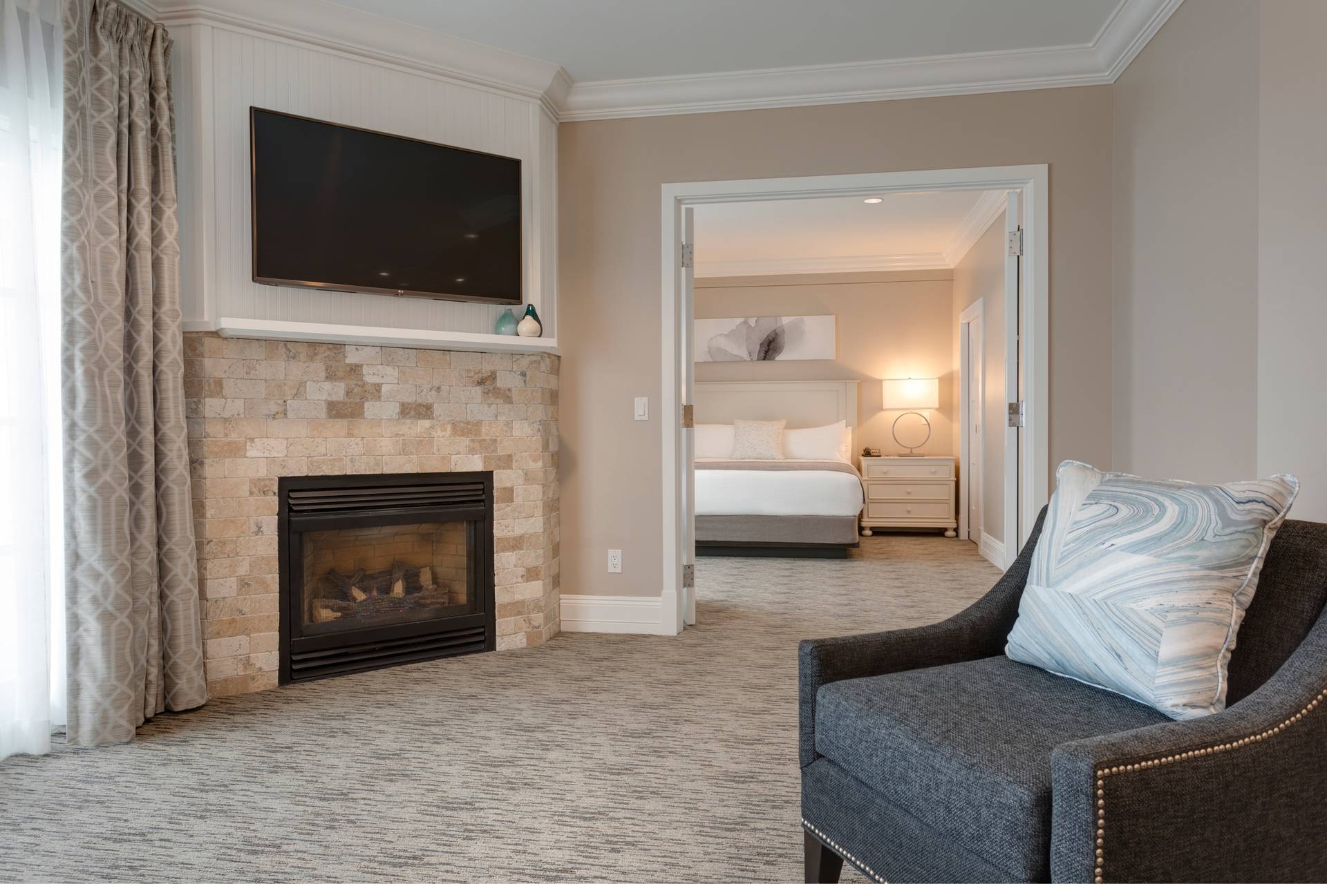 Dark armchair, tile fireplace near open king bedroom door of Specialty Suite, Inn at Bay Harbor