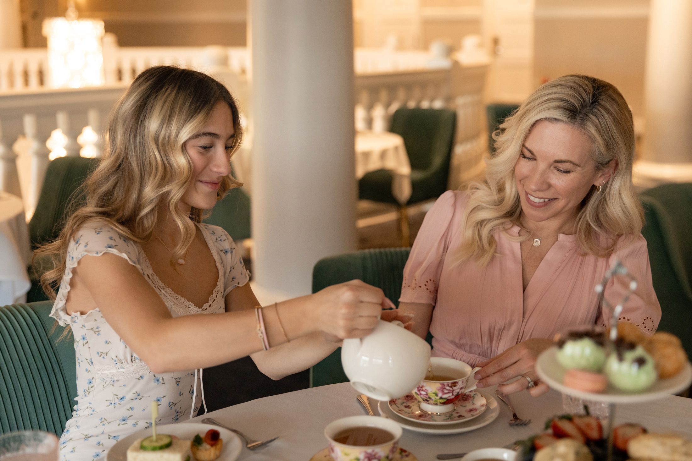 Teenage daughter pours tea into floral teacup with mother at Afternoon Tea service