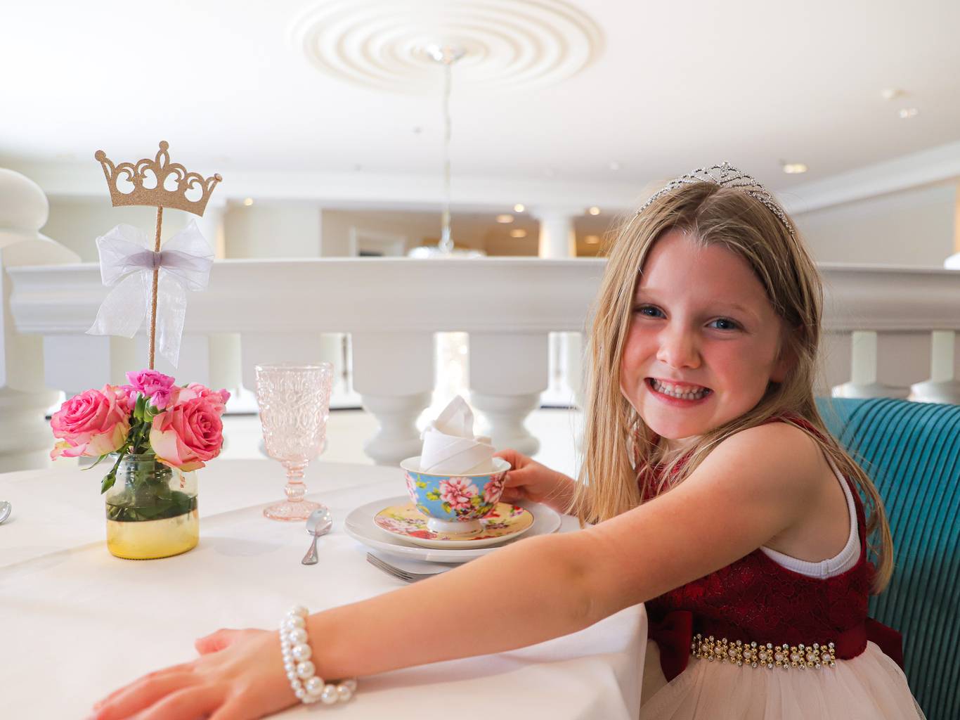Young girl dressed up with crown smiles with floral tea cup, Inn at Bay Harbor