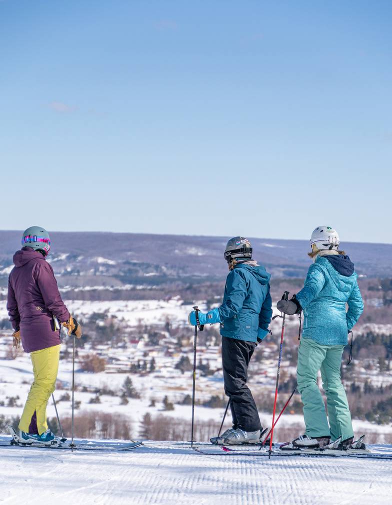Skiers look out on Boyne Valley from Boyne Mountain on clear blue sky day