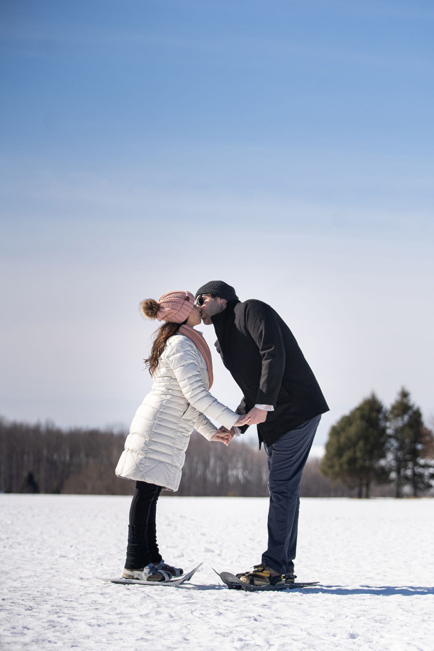 Snowshoeing couple in hats and winter coats kiss while holding hands