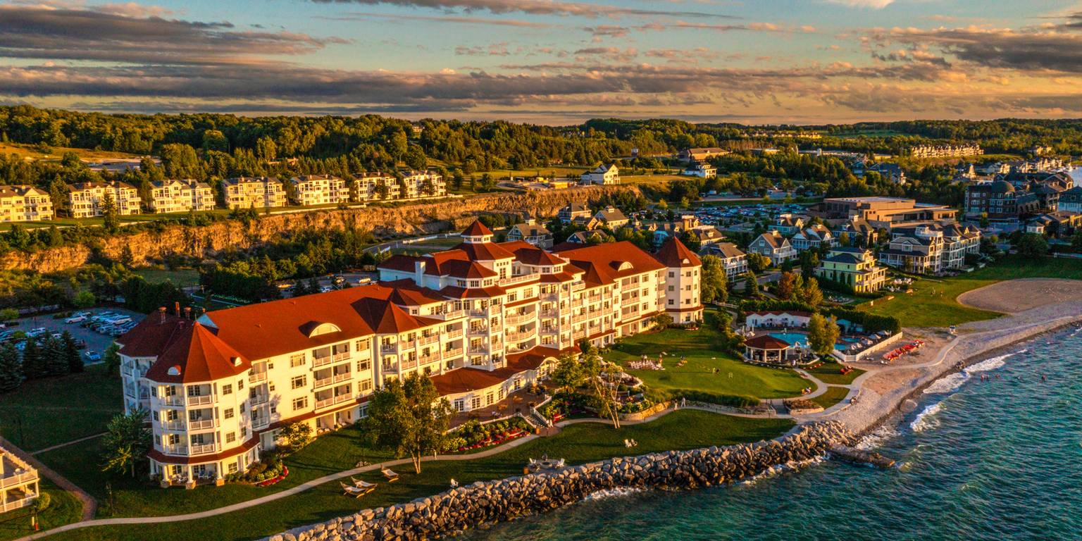 Aerial view of golden-tinted Inn at Bay Harbor hotel on Lake Michigan, with town background at sunset