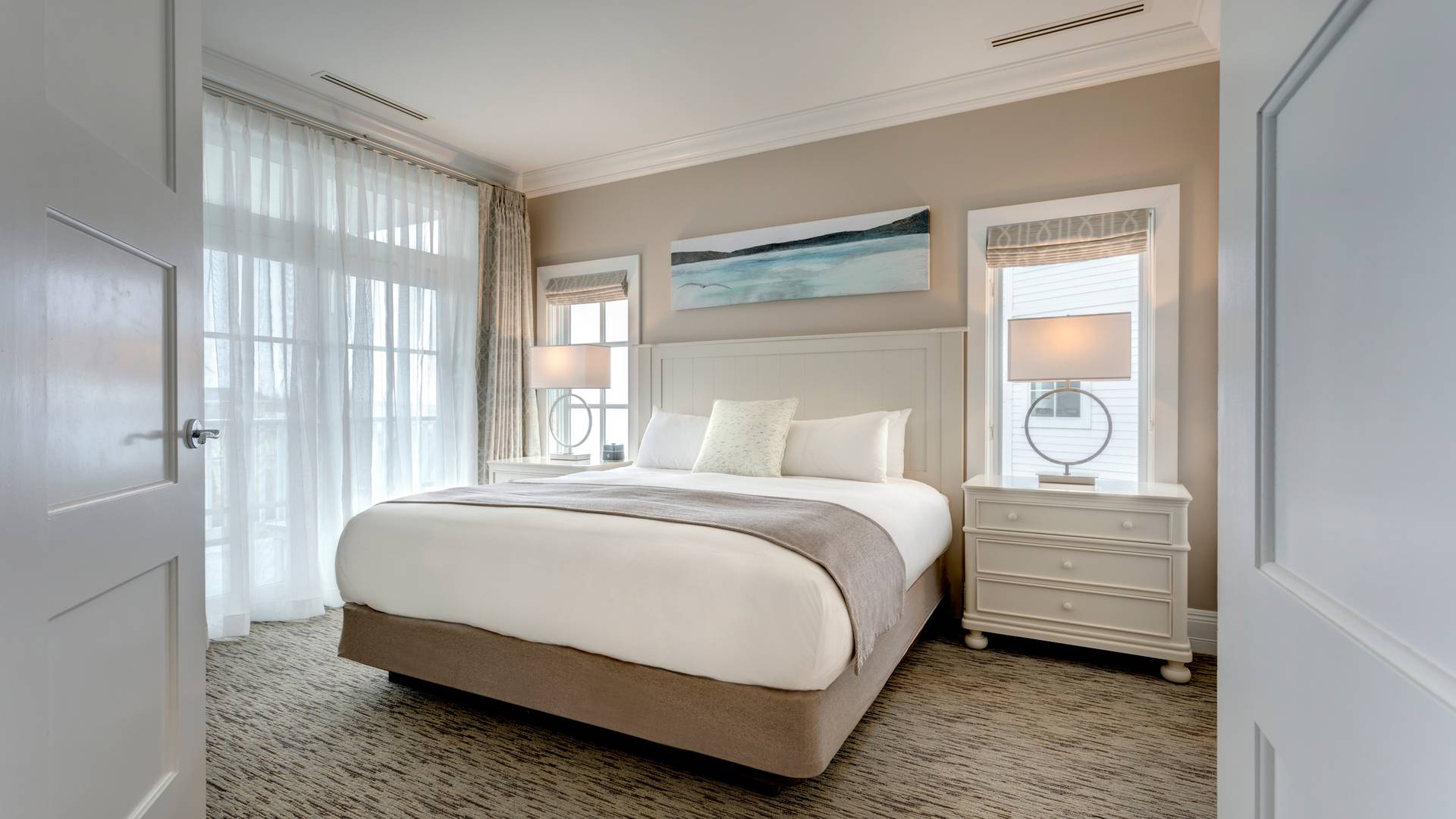 King Suite master bedroom with door slightly ajar, view of king bed, lamps, and large window