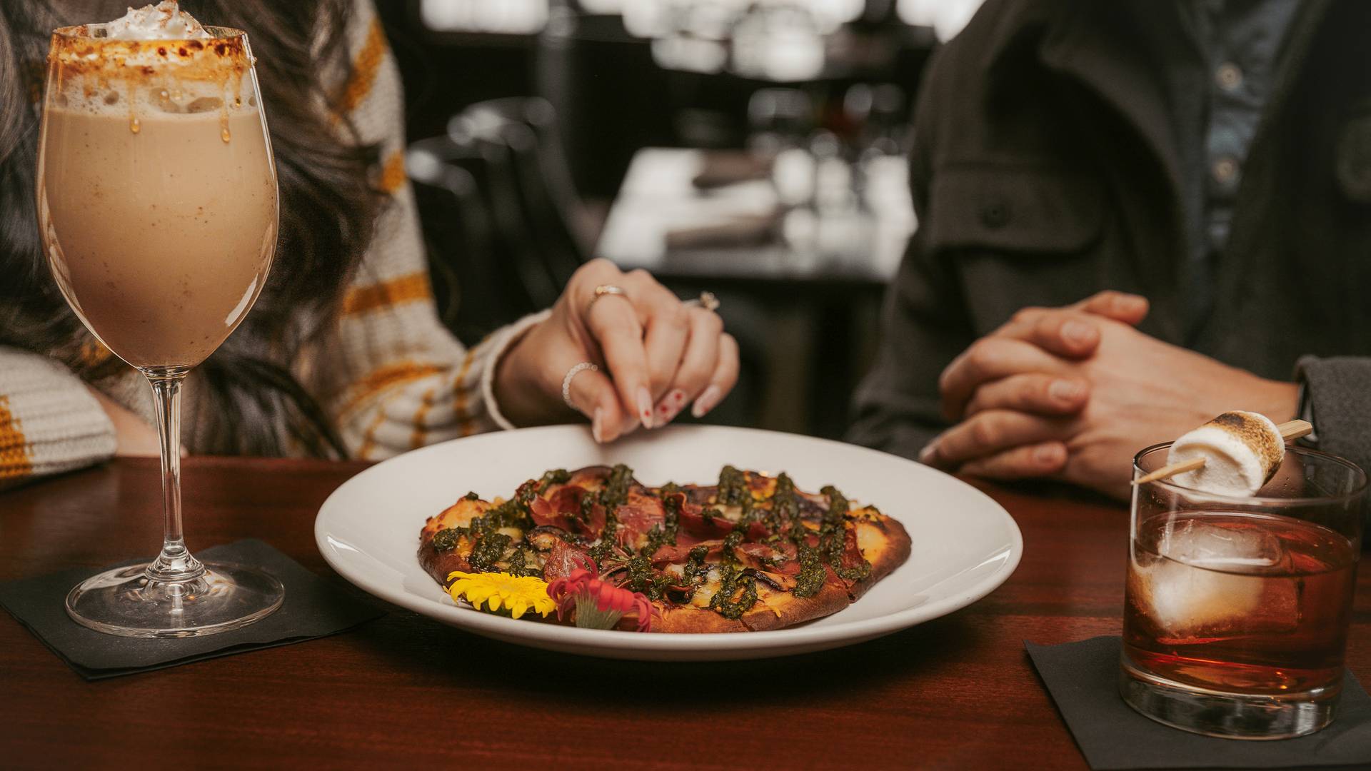 Couple shares colorful flatbread appetizer and specialty cocktails at bar