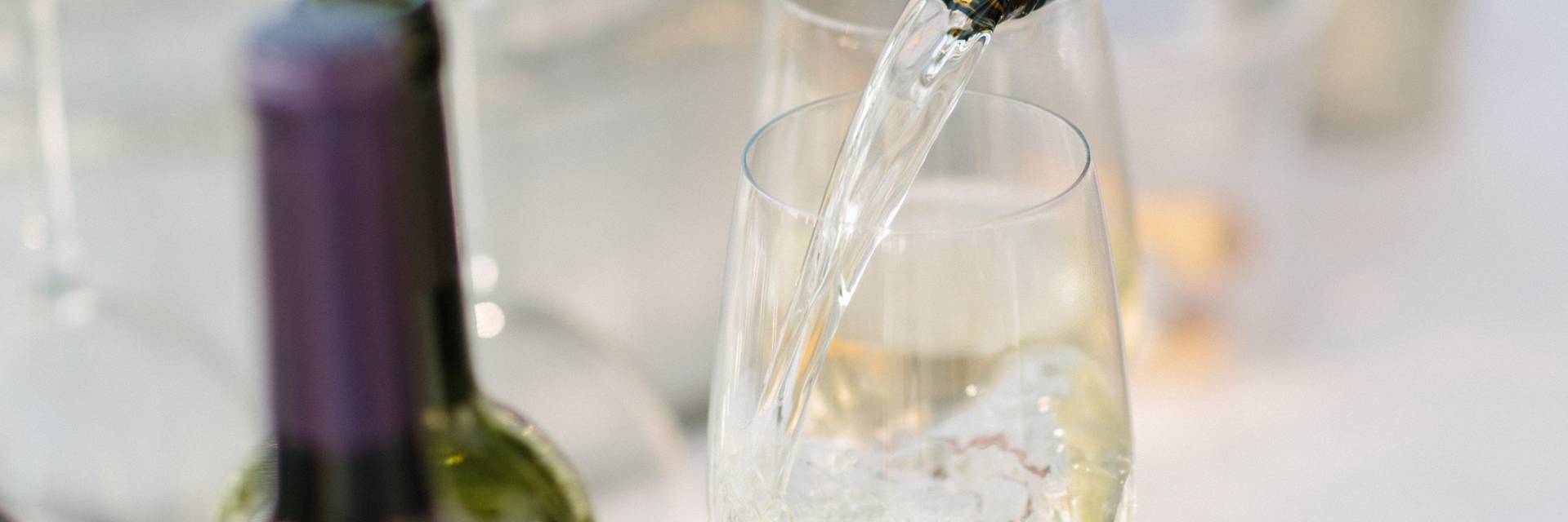 White wine pouring into glass, surrounded by bottles
