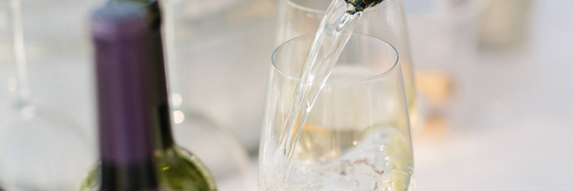 White wine pouring into glass, surrounded by bottles