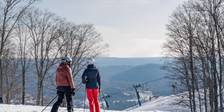 Ski couple looks out over valley view, chairlift from top of snowy slopes