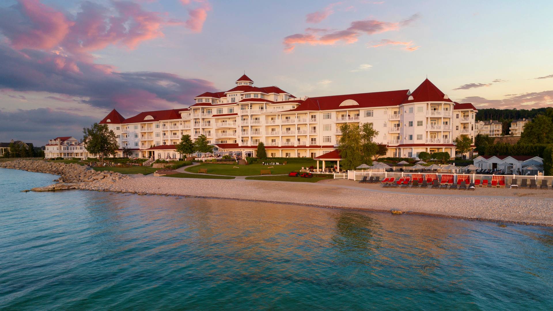 Golden hour exterior of Inn at Bay Harbor from water under pink and purple sunset sky
