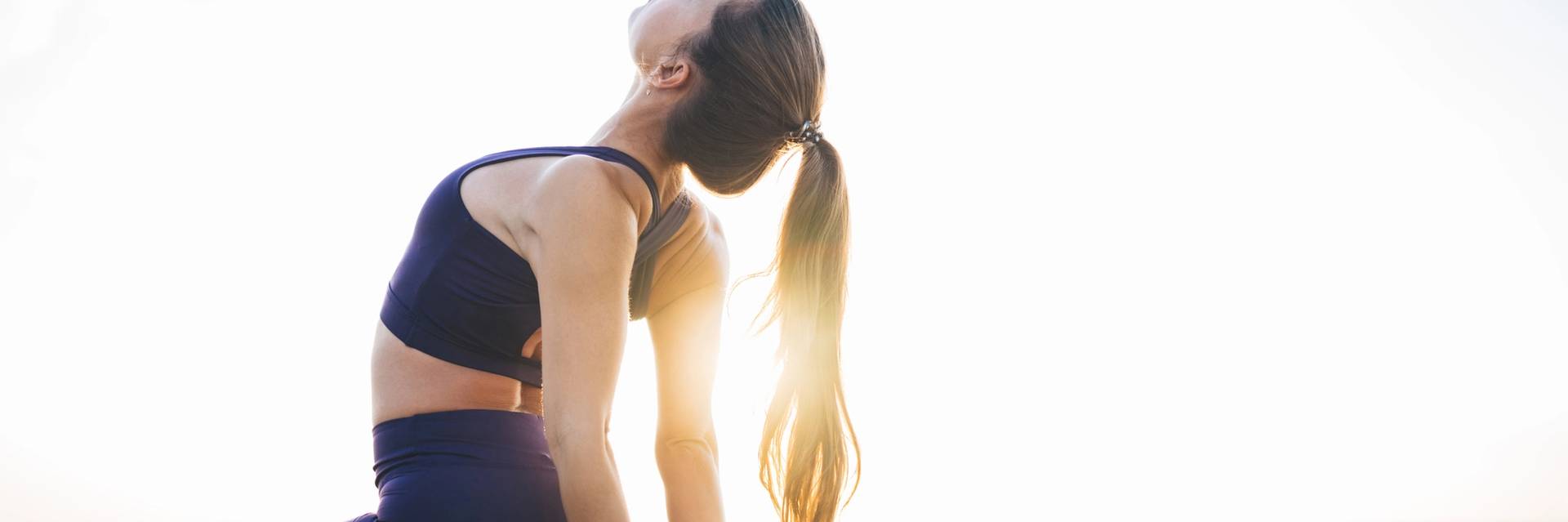 Young woman leans back on sunlit outdoor yoga mat