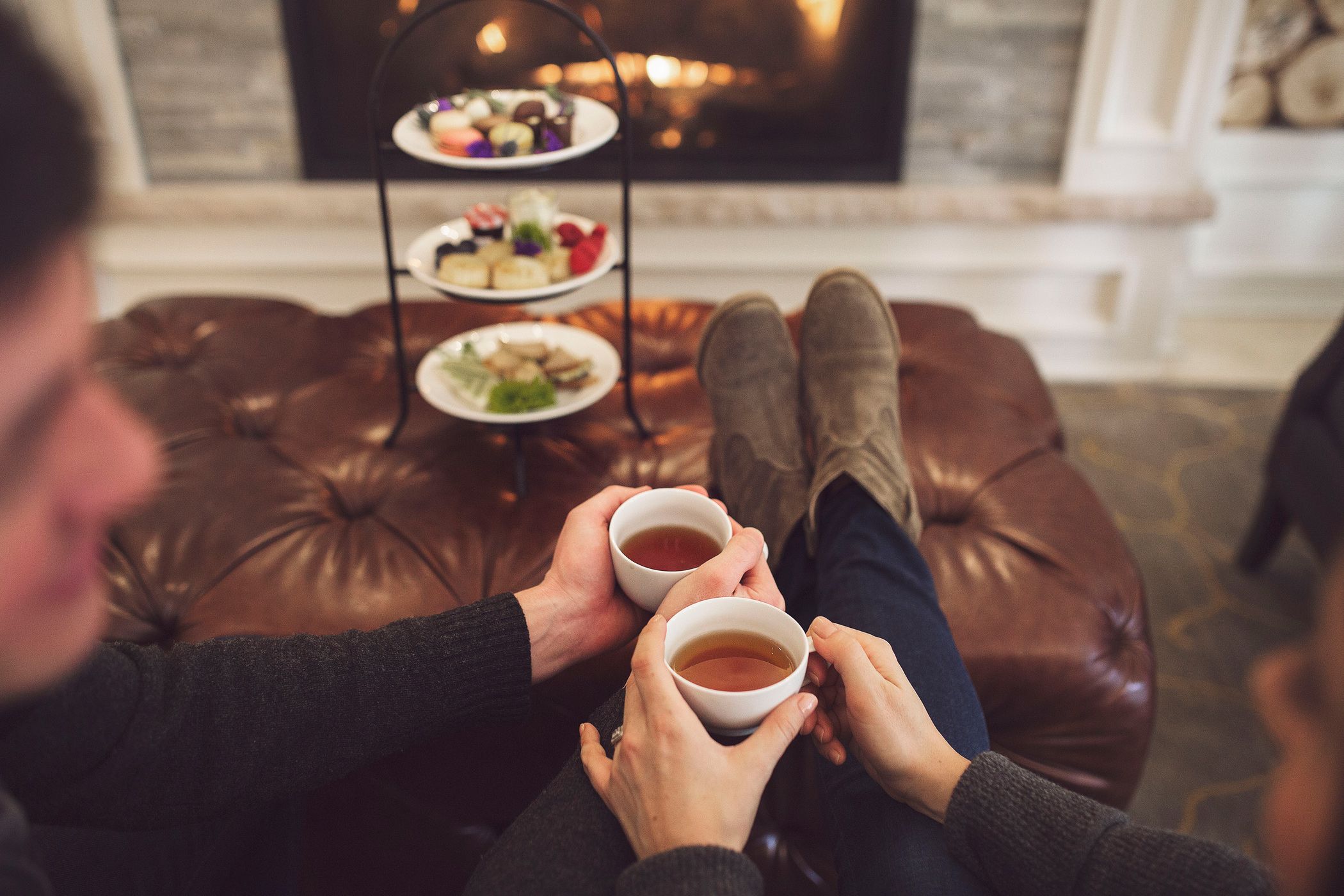 A couple sits together drinking tea in front of a fireplace