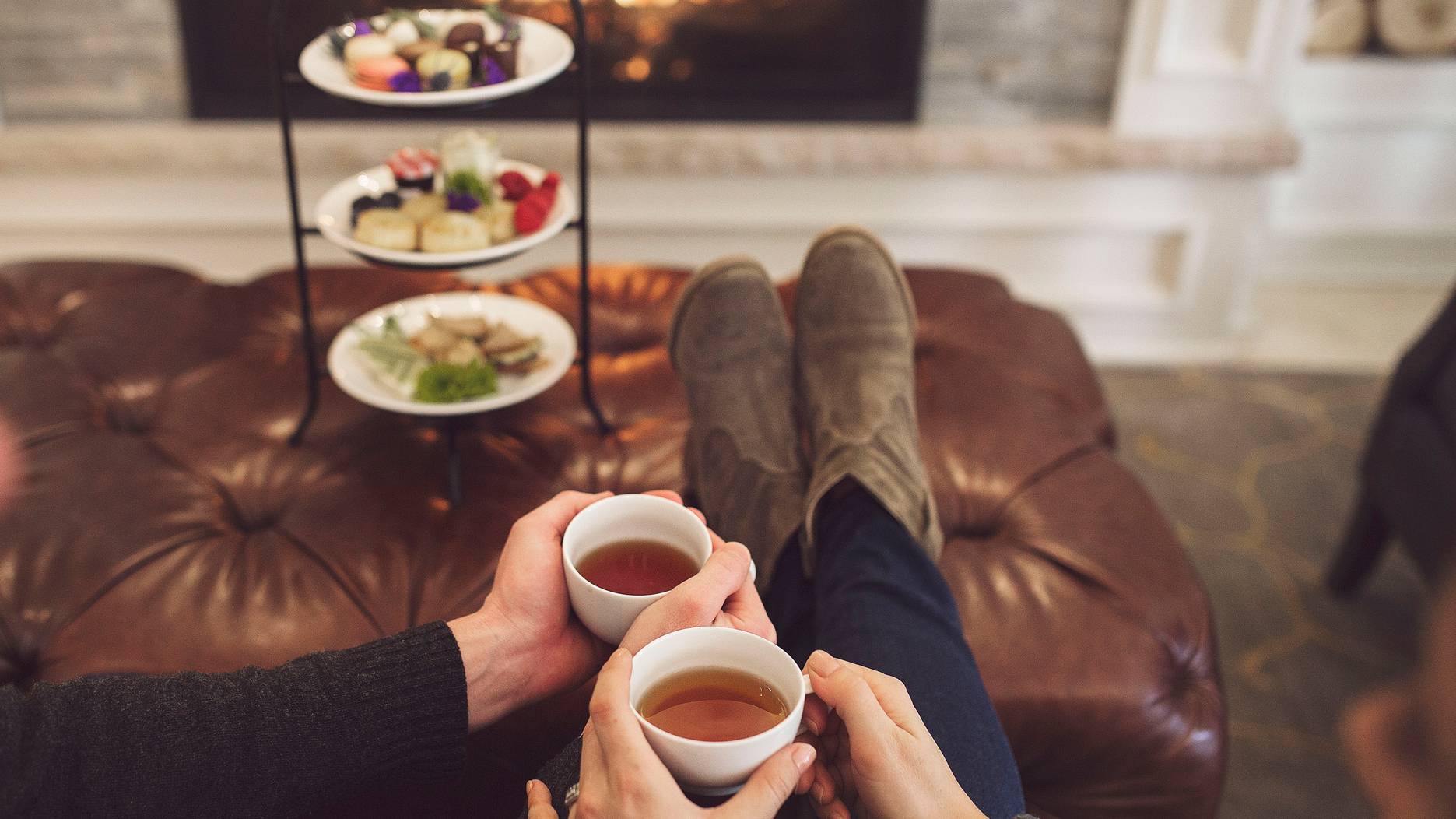 A couple sits together drinking tea in front of a fireplace