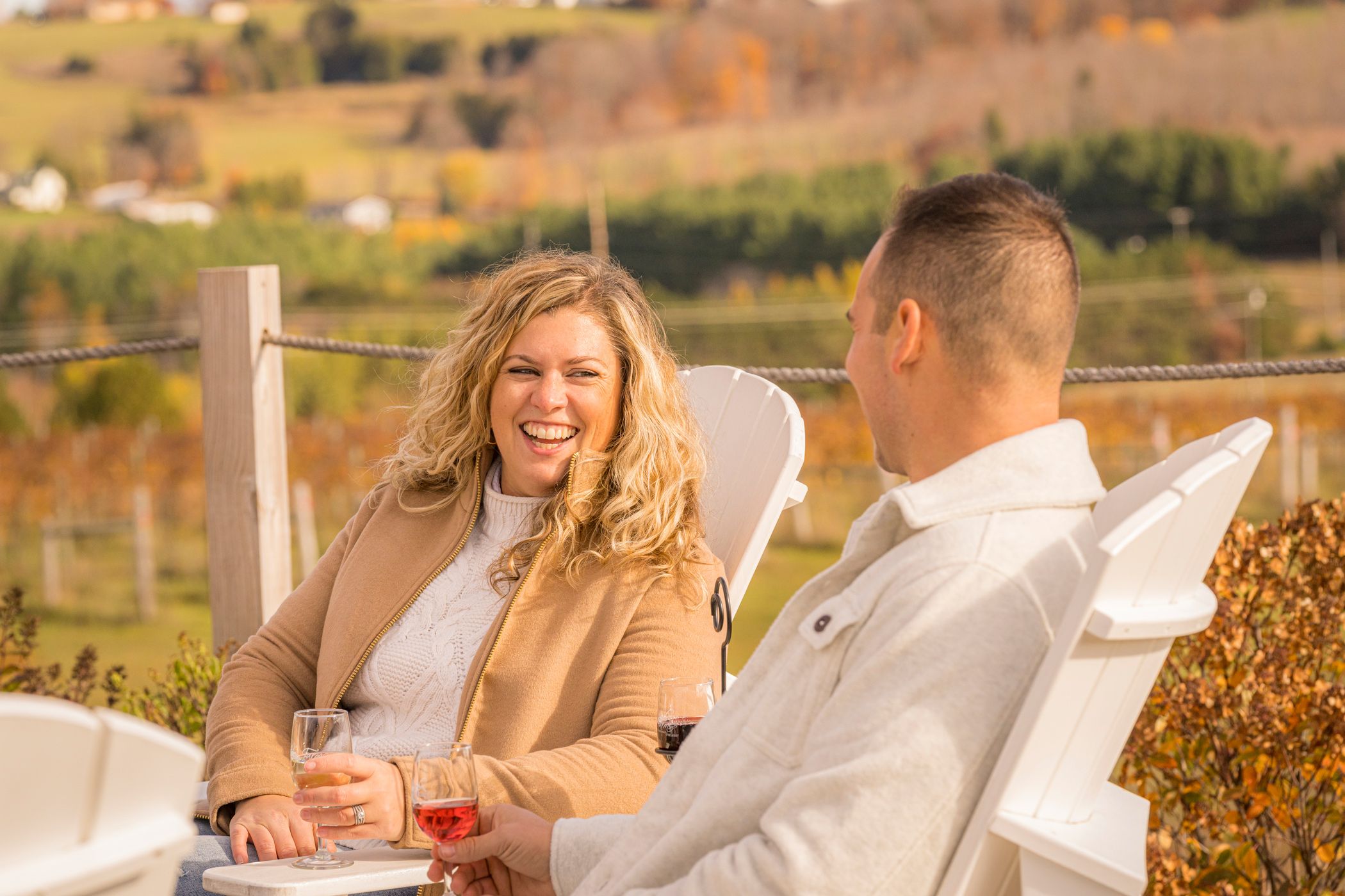 A woman laughs while drinking wine with a man at a vineyard