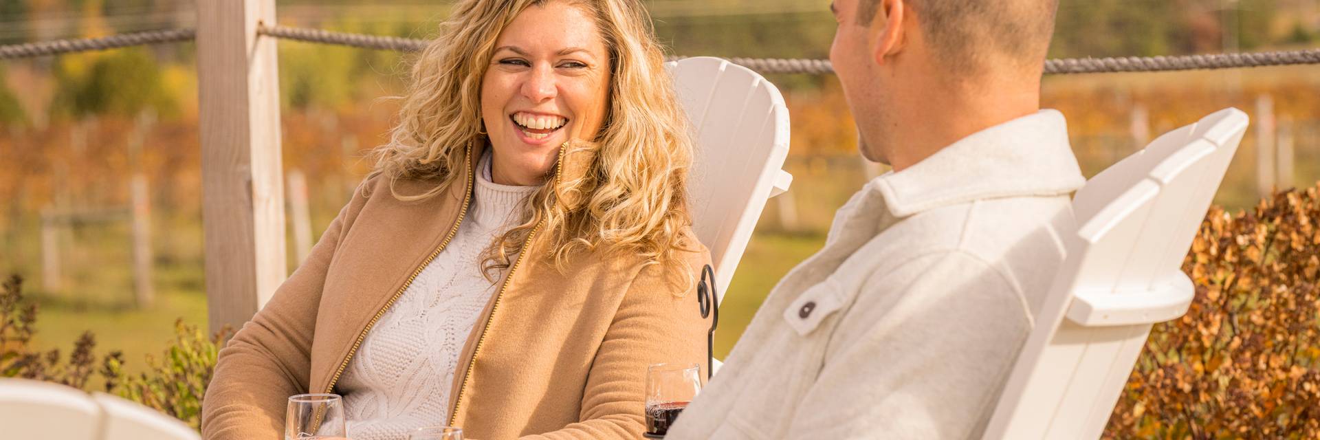 A woman laughs while drinking wine with a man at a vineyard