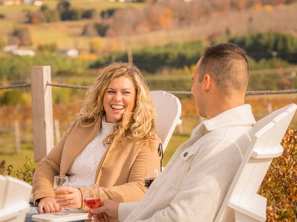 A woman laughs while drinking wine with a man at a vineyard