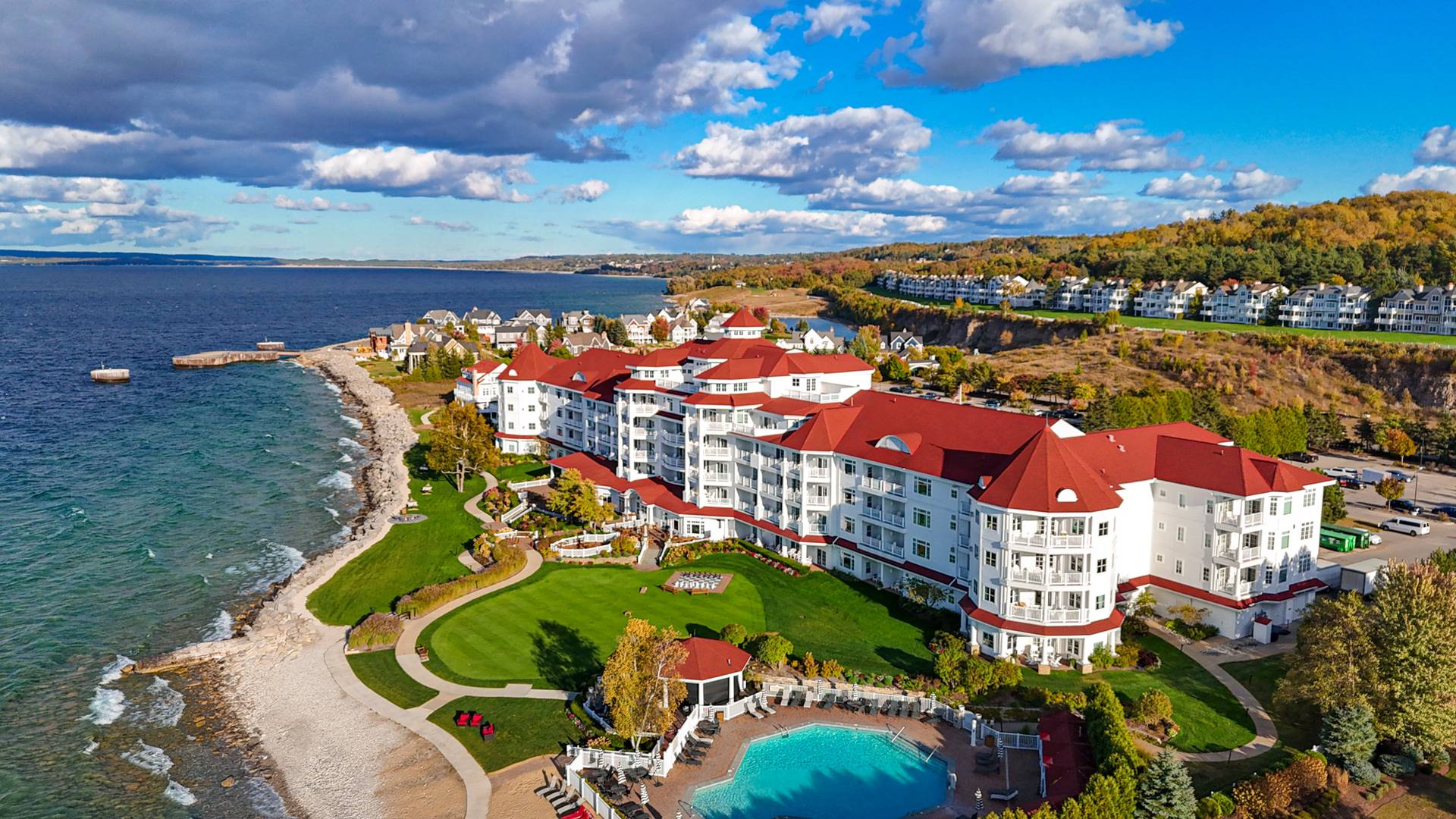 Aerial view of autumn lakefront exterior of Inn at Bay Harbor, featuring fluffy clouds, changing tree landscape