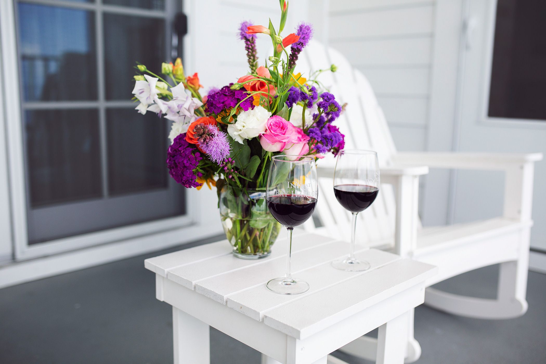 Two glasses of red wine, colorful flower bouquet, on Inn at Bay Harbor balcony.
