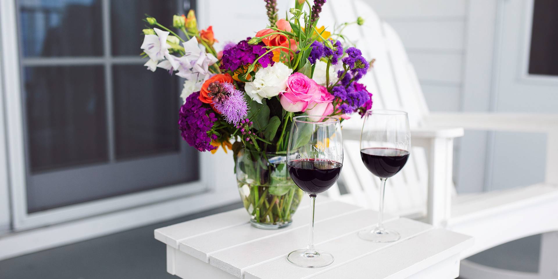 Two glasses of red wine, colorful flower bouquet, on Inn at Bay Harbor balcony.