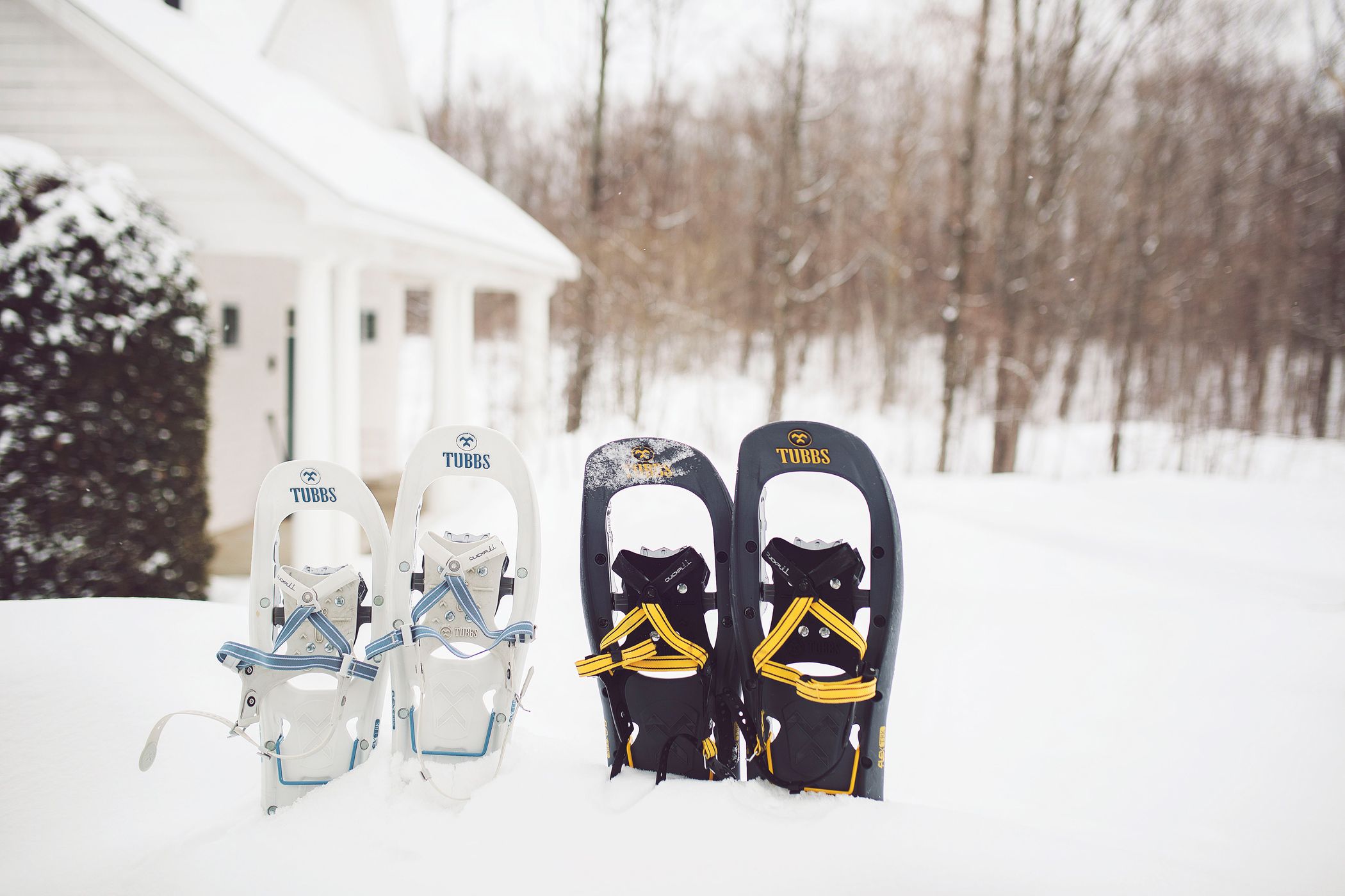 White and black Tubbs snowshoes in snowbank near winter woods and cottage