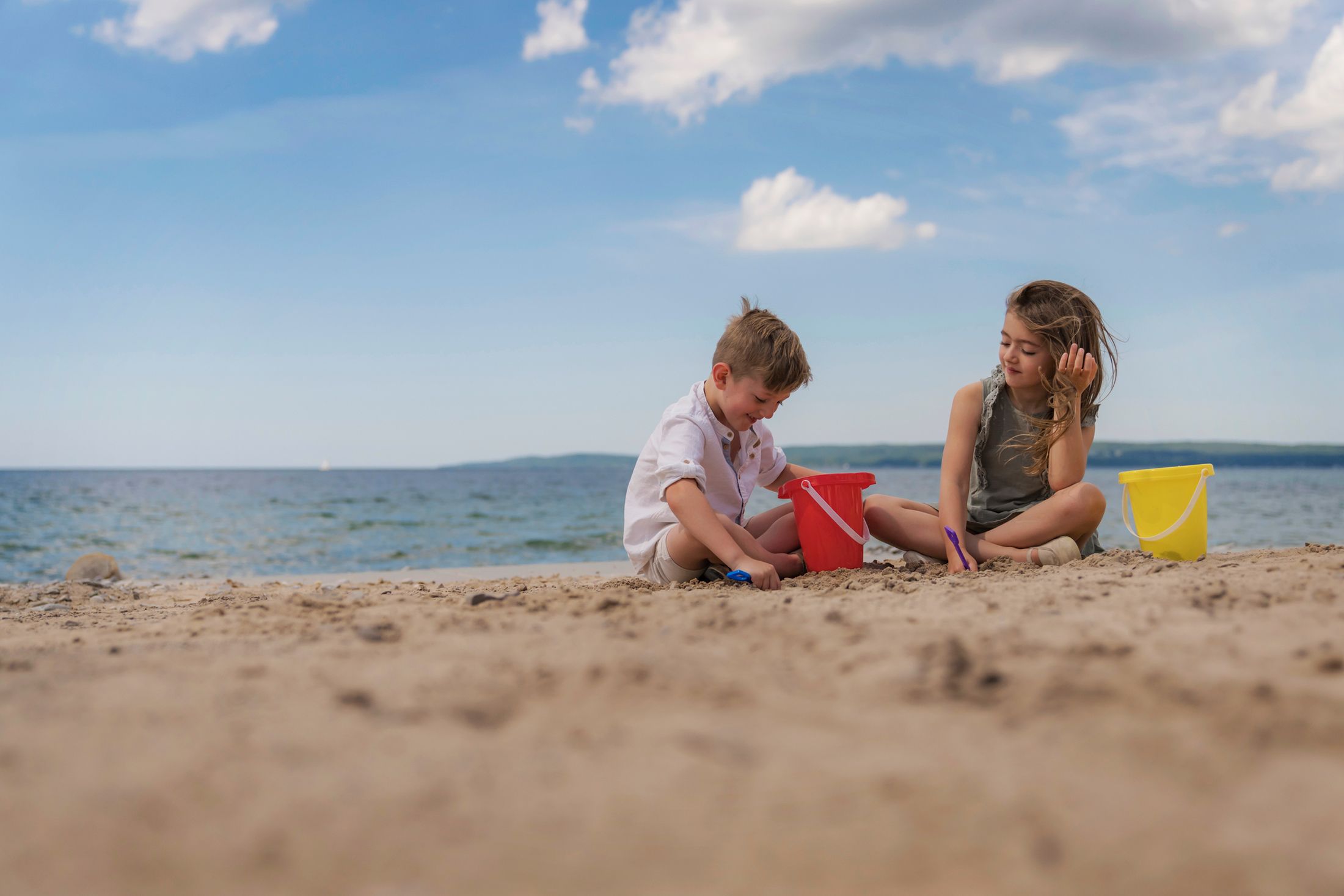 Two children play on Lake Michigan beach with sand toys and buckets