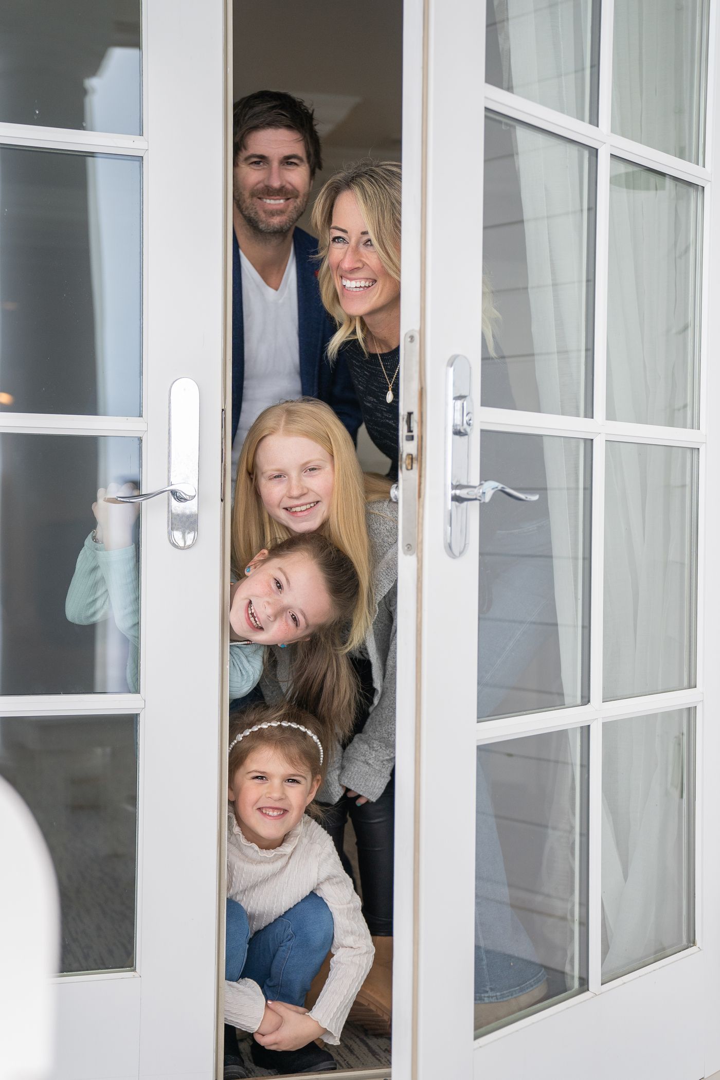 Smiling family looks out onto winter balcony through French doors